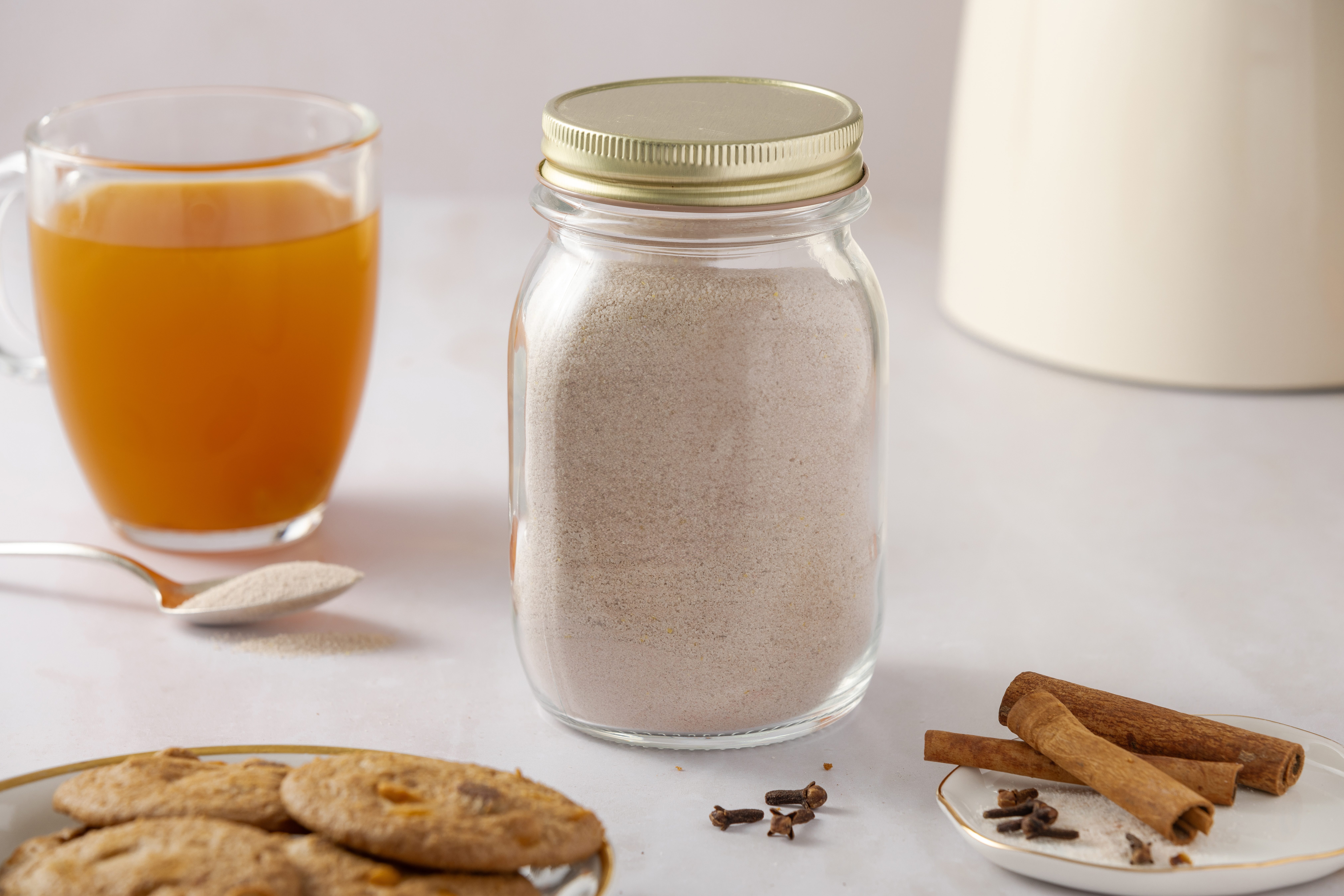 Spiced tea mix in air tight container, with drink in the background.