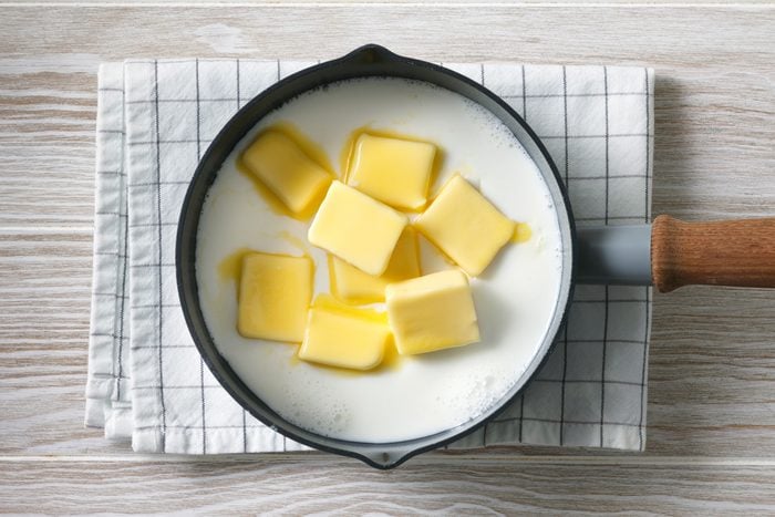 Overhead shot of a small saucepan; heat milk and butter until just warm and butter is melted; set aside; napkin; wooden surface;