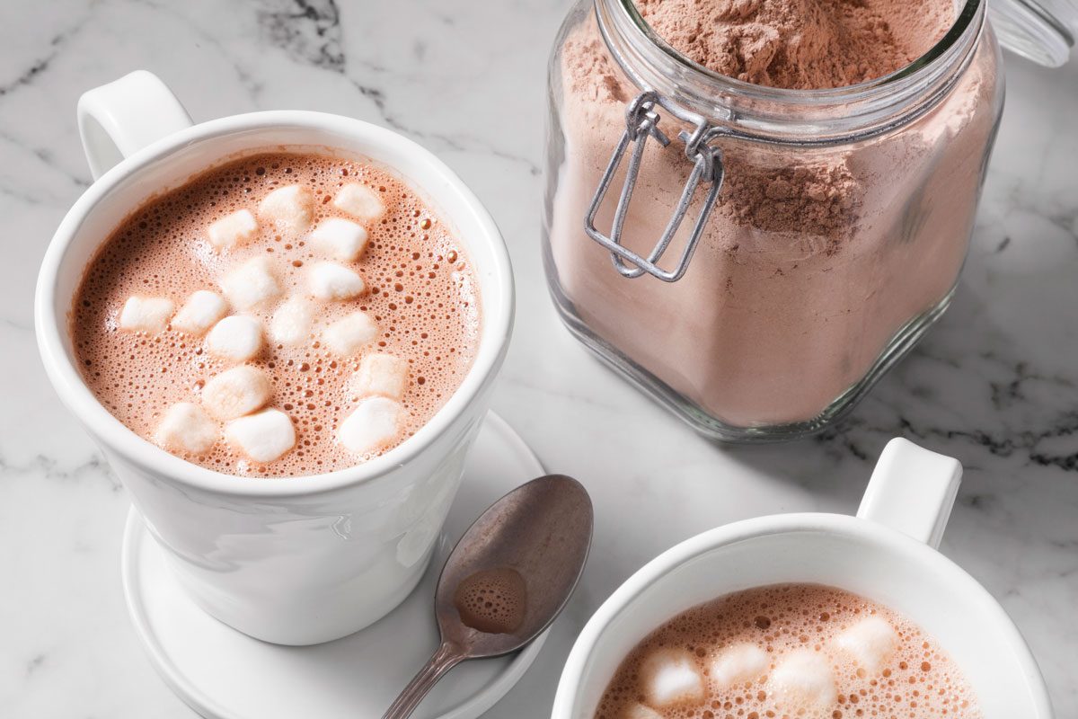 high angle shot of hot cocoa mix in a jar and two cups of hot coco