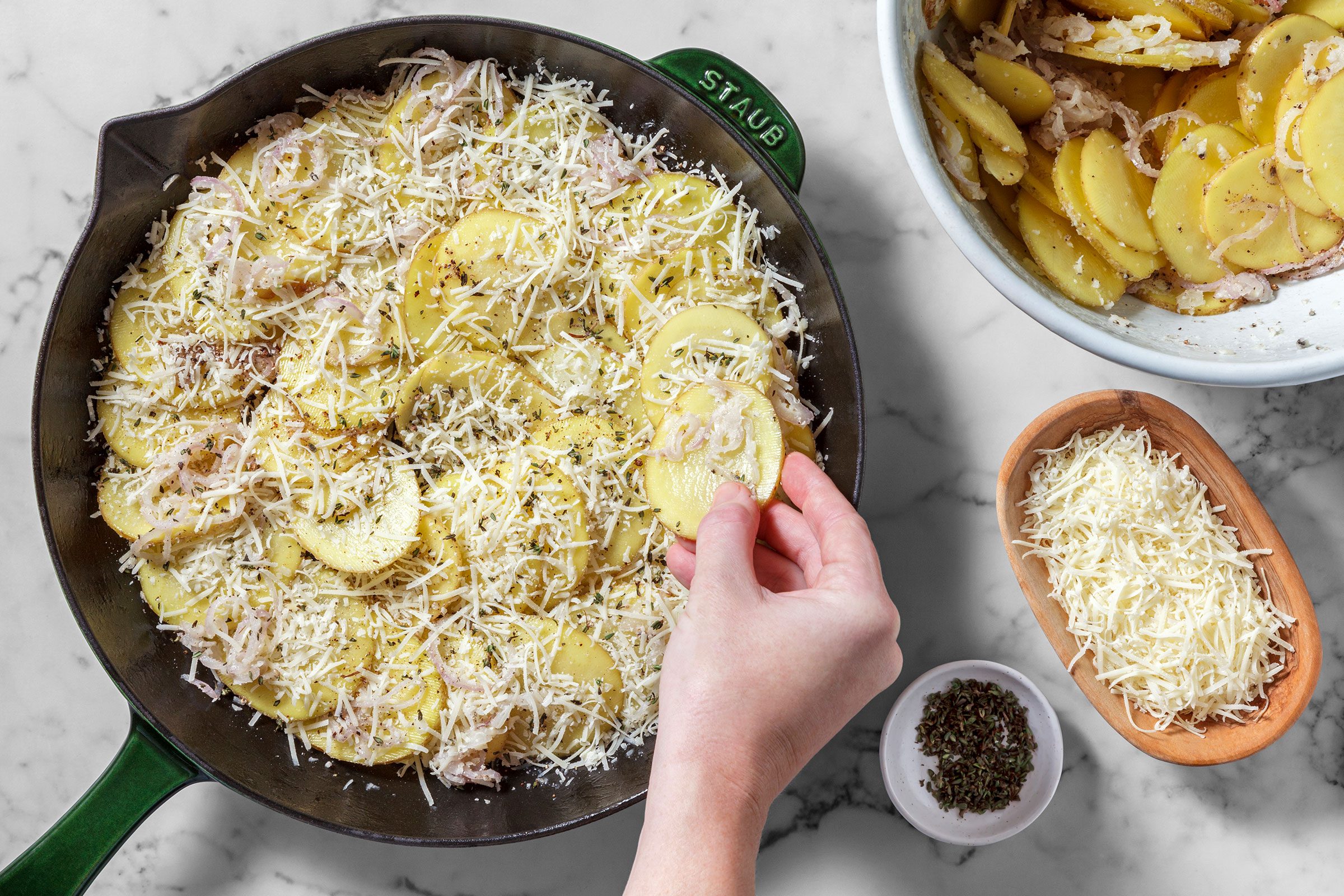 Potato slices and shallots in a large skillet with seasonings and grated cheese on top