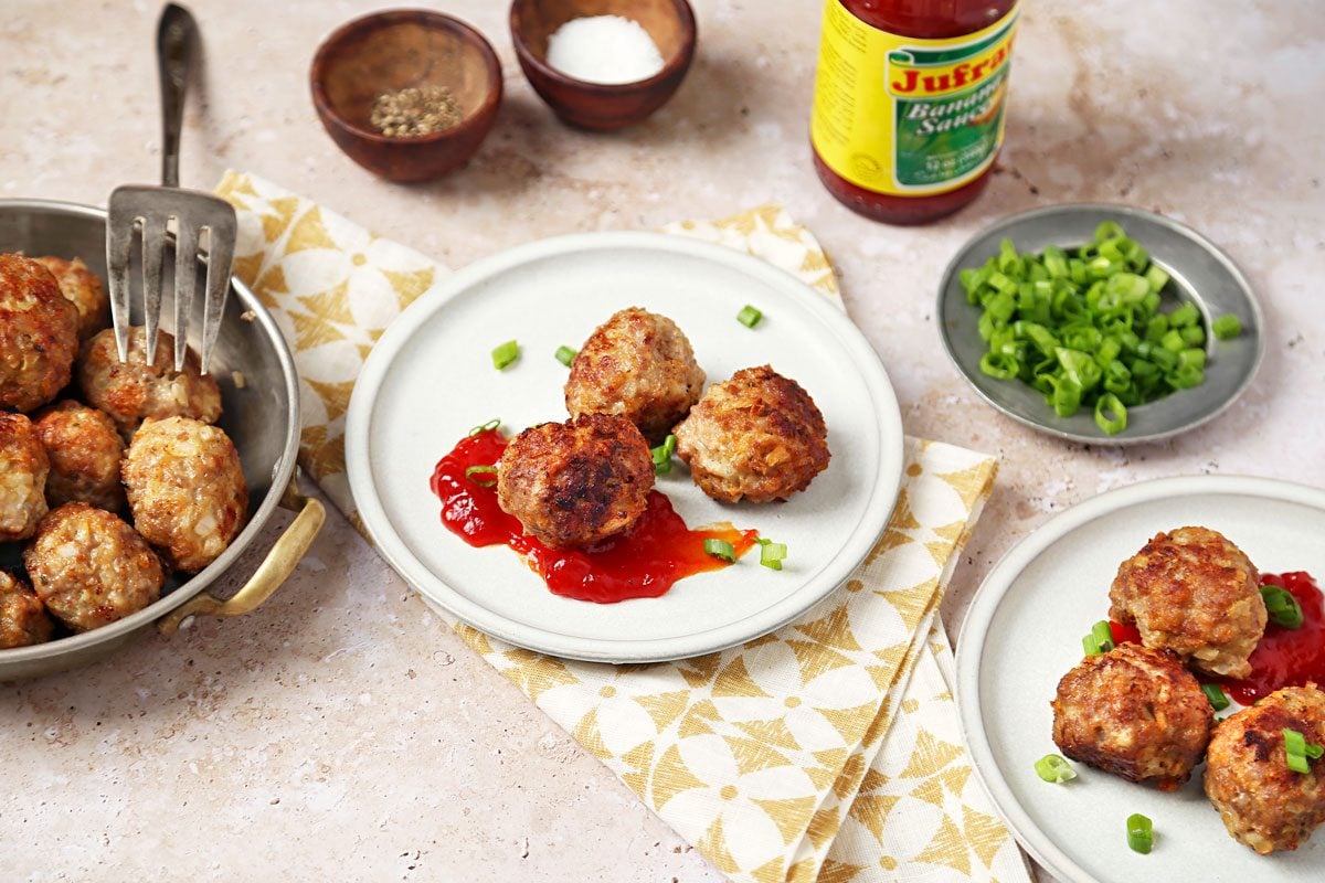 Bola Bola 3/4th shot on a beige marble surface. Meatballs served on little stone plates with banana ketchup.