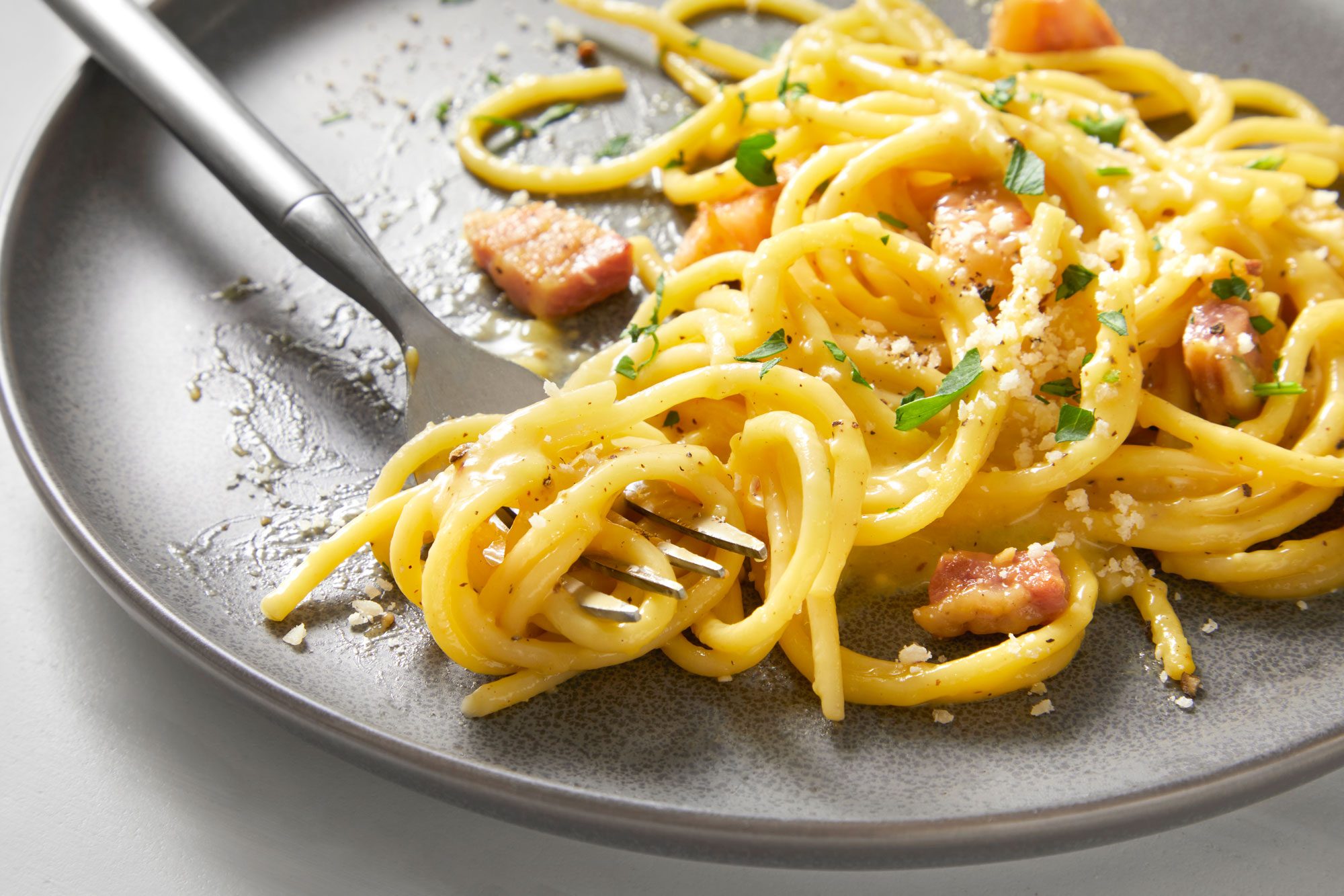 A plate of carbonara spaghetti topped with crispy bacon and fresh herbs served with fork