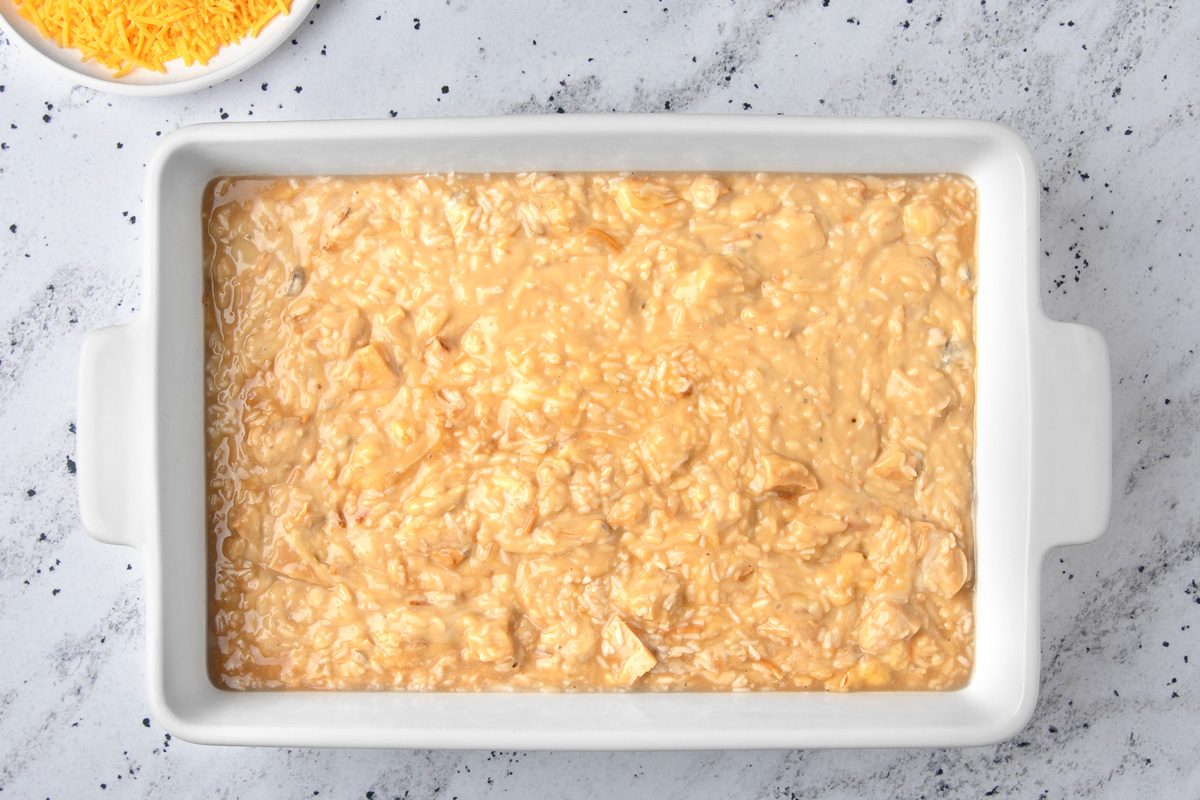 overhead shot of a white rectangular baking dish filled with a mixture of cooked rice, chicken, and a creamy sauce; the dish is sitting on a light gray speckled countertop