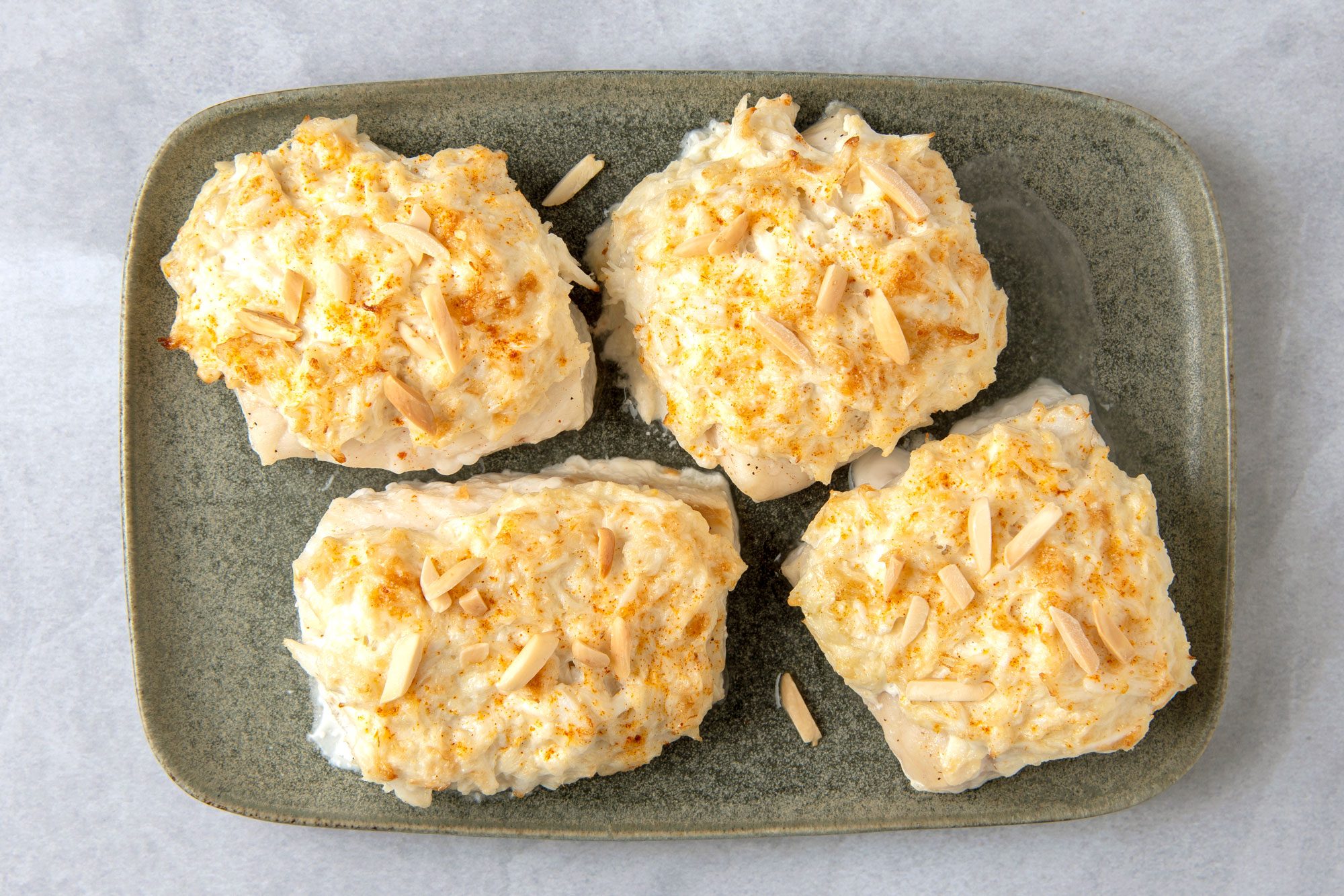 Four pieces of Crab-Topped Fish on a green plate and each piece is topped with a creamy sauce and sliced almonds