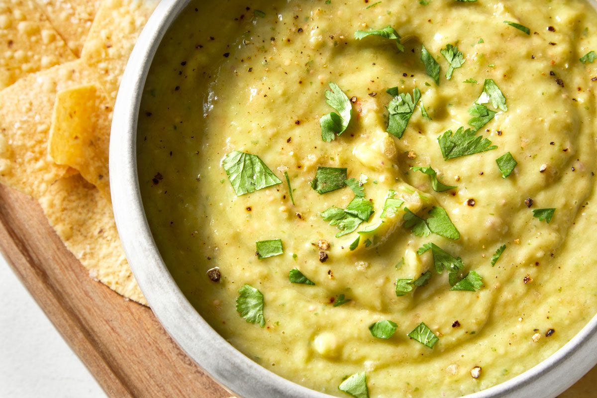 overhead closeup shot of a bowl of Guacamole Salsa, served with crispy tortilla chips; the bowl is placed on a wooden cutting board