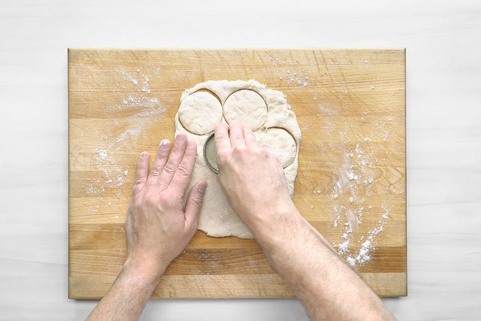 Overhead shot of pat dough to 1/2-inch thickness; cut with a 2-1/2-inch biscuit cutter; wooden board; wooden surface