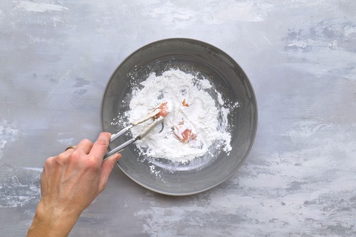 Tossing and coating marinated chicken pieces in cornstarch in a skillet