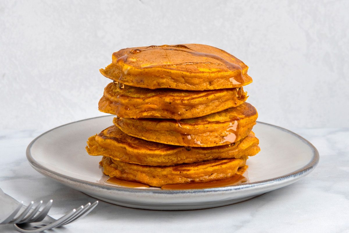 Table view shot of Fluffy Sweet Potato Pancakes; served on plates; with syrup; forks; marble surface;