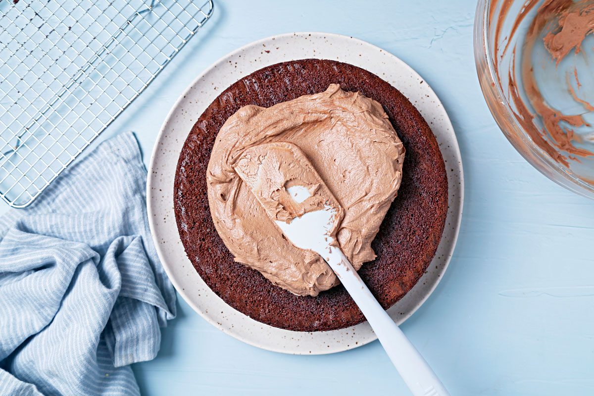 Round vegan cake on a serving platter with vegan chocolate frosting on top.