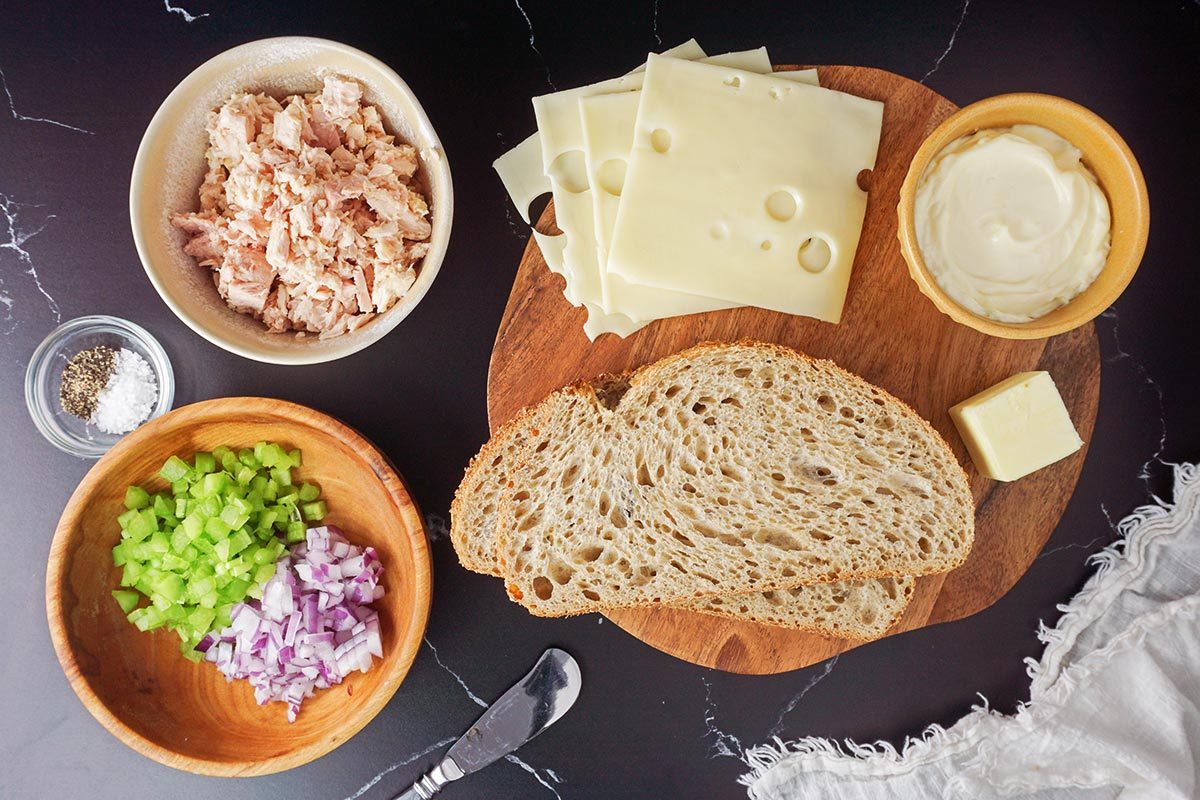 Ingredients for a tuna melt on a wooden cutting board and a black stone countertop