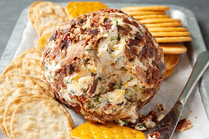 Close shot of Bacon Ranch Cheese Ball; on a platter with assorted crackers; knife; grey surface