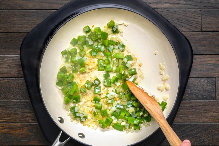 overhead shot of diced green peppers, onions, and minced garlic being sauteed in a white pan