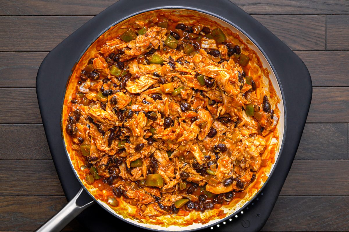 overhead shot of a white skillet filled with a mixture of shredded chicken, black beans, and green bell peppers