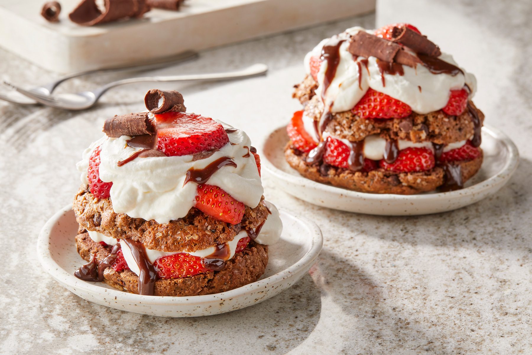 Table view shot of Chocolate Strawberry Shortcakes; garnished with chocolate; served on two plates; forks; marble surface;