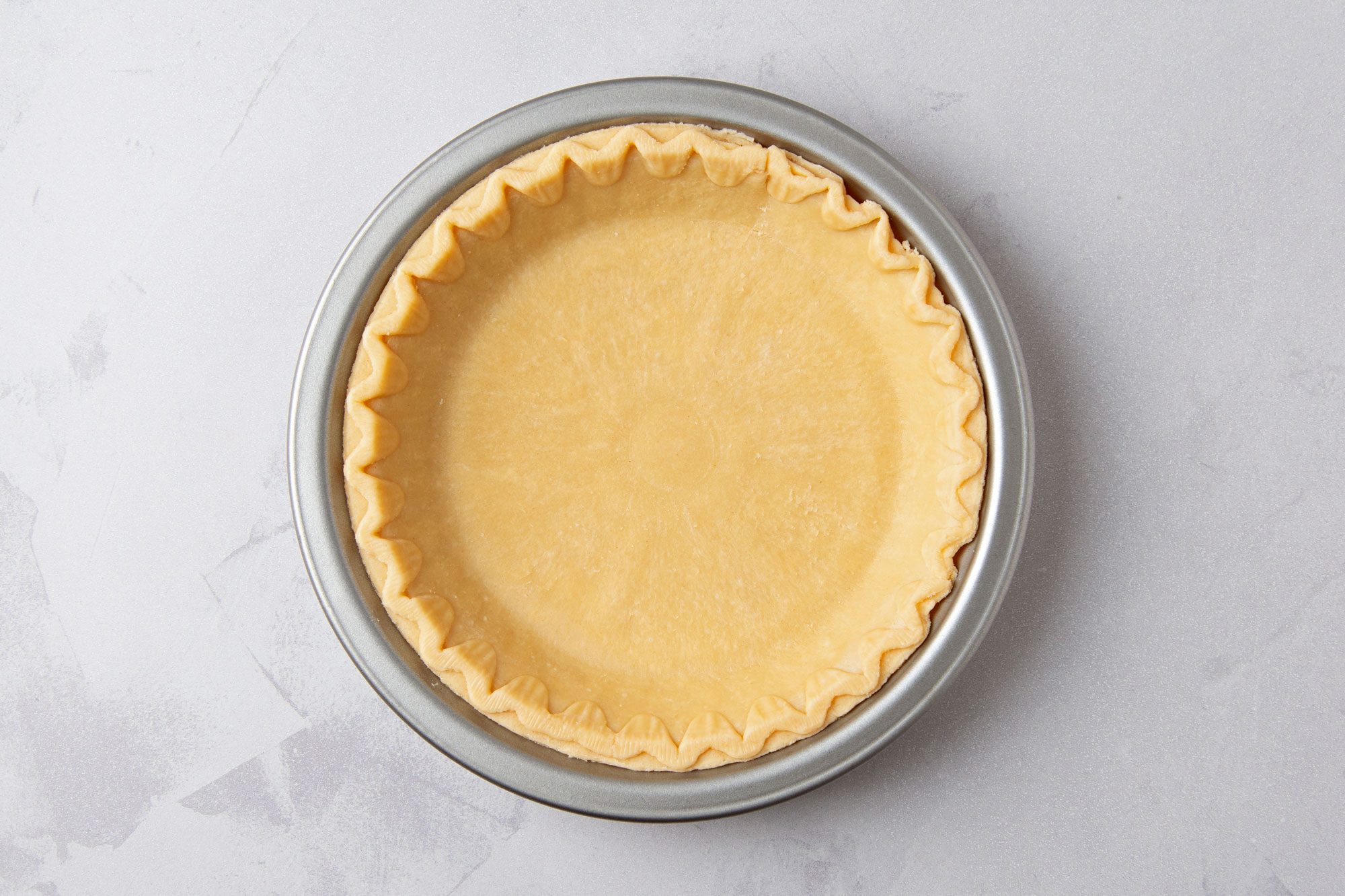 overhead shot of of a pie crust in a metal pie pan on a light gray countertop
