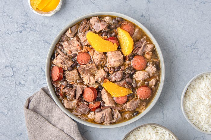 A bowl of feijoada, a Brazilian stew containing black beans, pork, and sausage, garnished with orange slices.