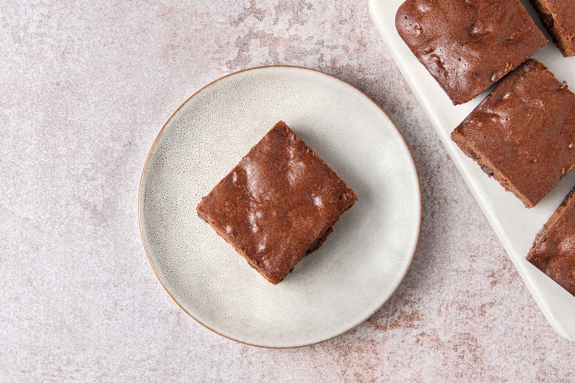 Overhead shot of Easy Gluten Free Brownies; place on white tray; served on a small plate; light brown marble surface;