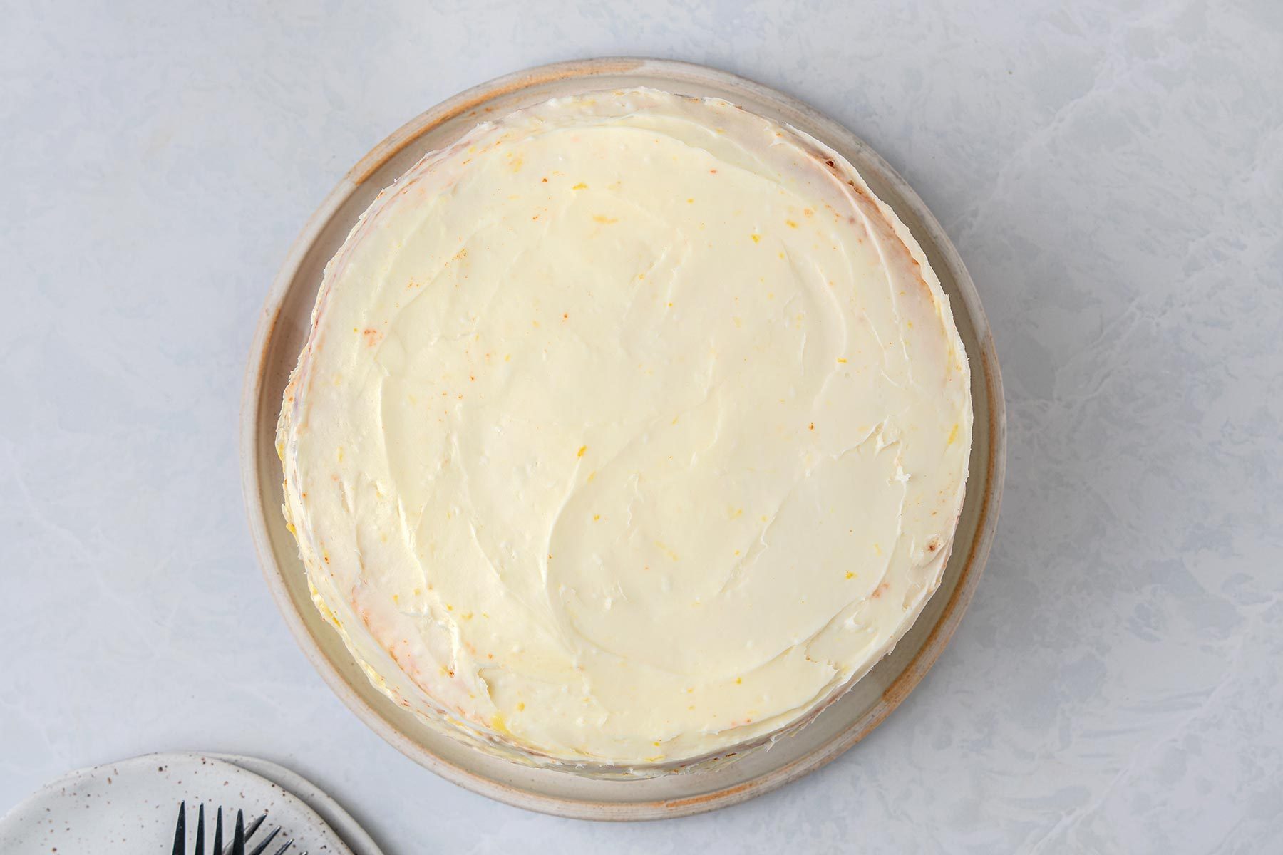 Evenly spread the frosting over cake kept on top of a grey marbletop.