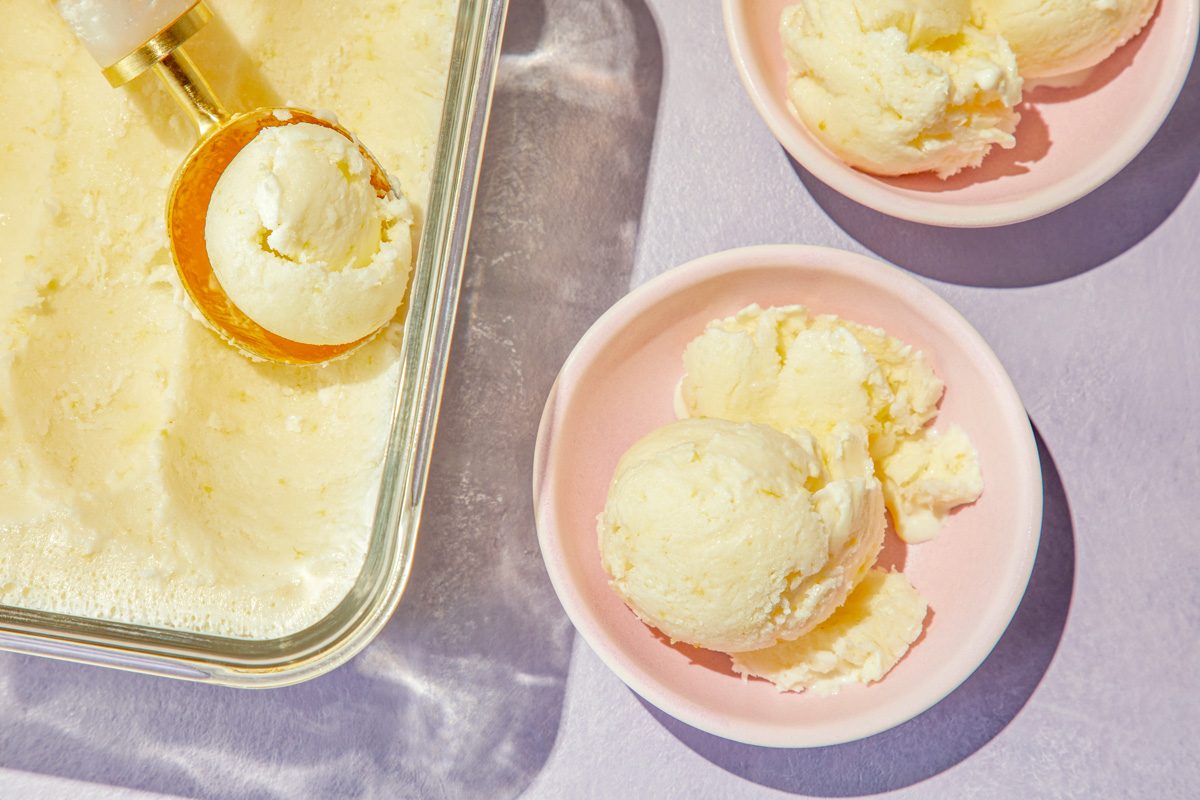 overhead shot of Lemon Sherbet served in a transparent glass. Next to the main dish, there are two pale pink bowls, each showcasing scoops of lemon sherbet
