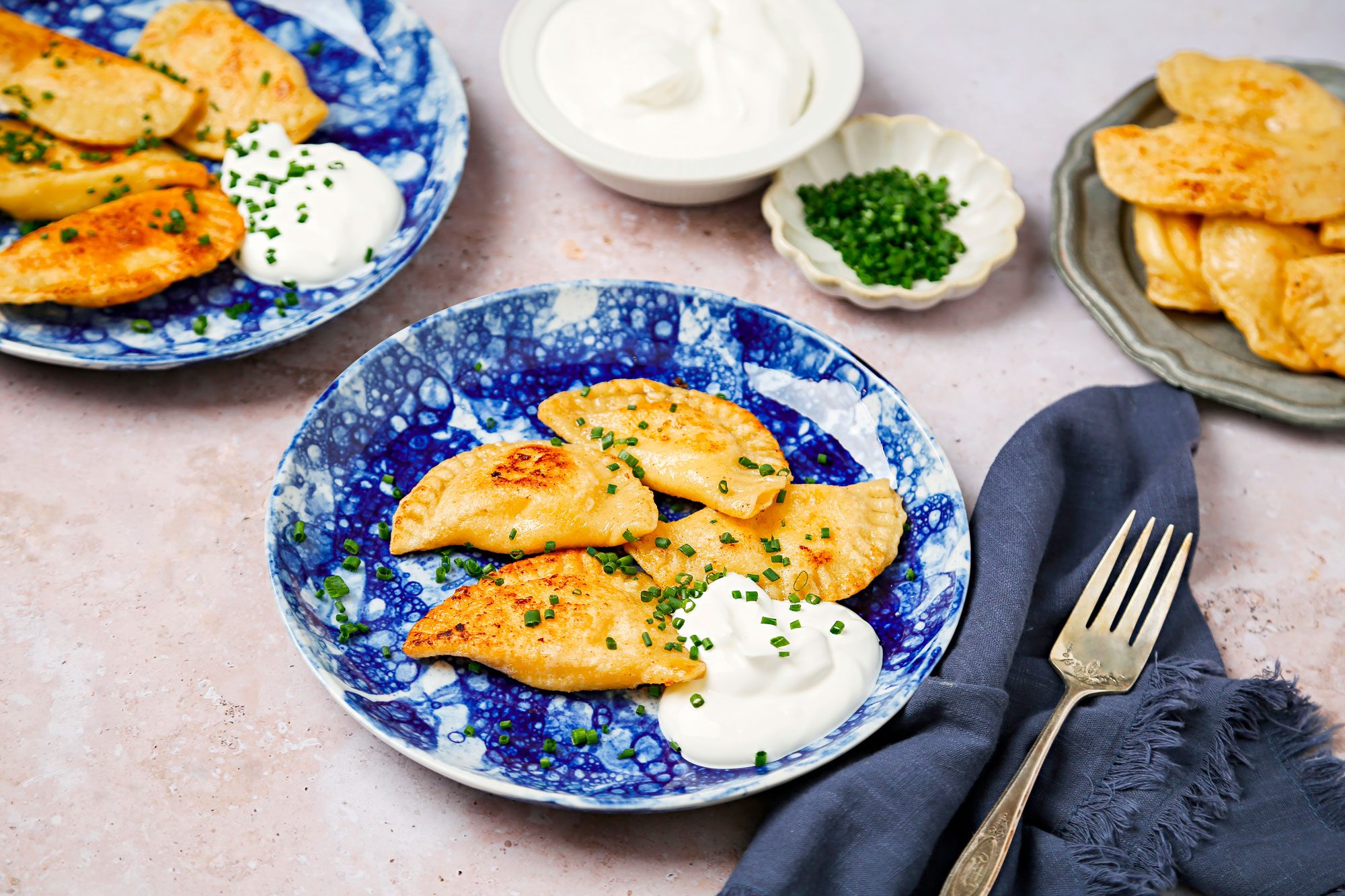 Sauteed pierogi served on blue and white plates with sour cream and chives