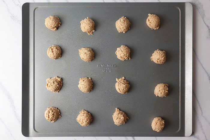 A baking tray with 15 evenly spaced unbaked cookie dough balls on a marble countertop.