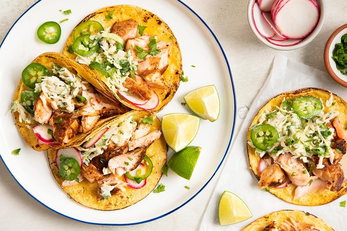 Salmon taco served on a plate and lime wedges on the side.