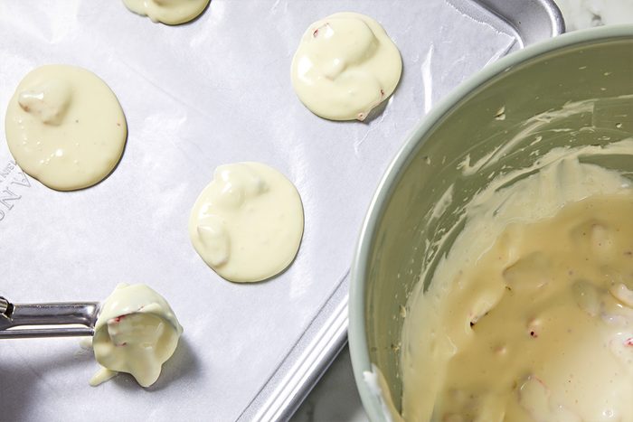 Overhead view of scooping the cream cheese filling onto a parchment paper-lined baking sheet. Next to it lies the large bowl containing the filling.