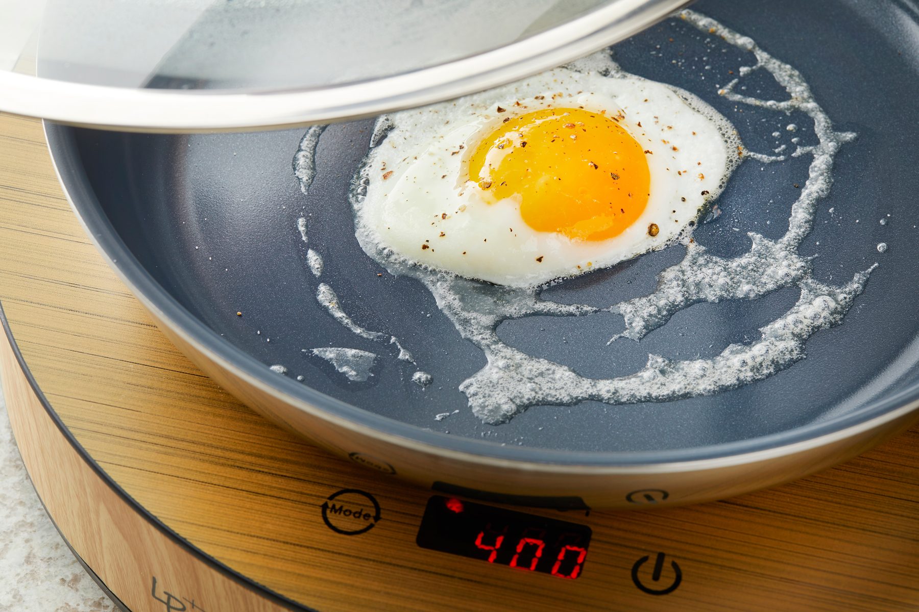 Close shot of cover; and reduce heat to medium-low; cook 2-3 minutes or until whites are fully set and yolks are runny; induction; marble surface;