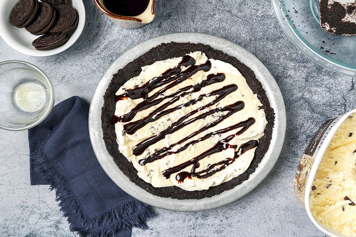 Ice cream layer with chocolate syrup drizzle on crust for prepping mud pie with Oreo in a bowl