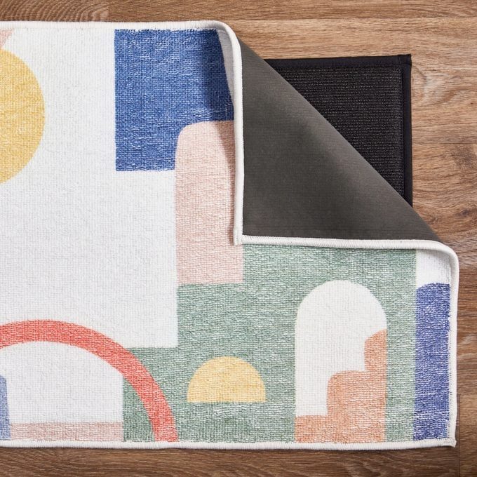 Multicolored Ruggable bathmat folded back to reveal a black rug mat on a brown wood floor