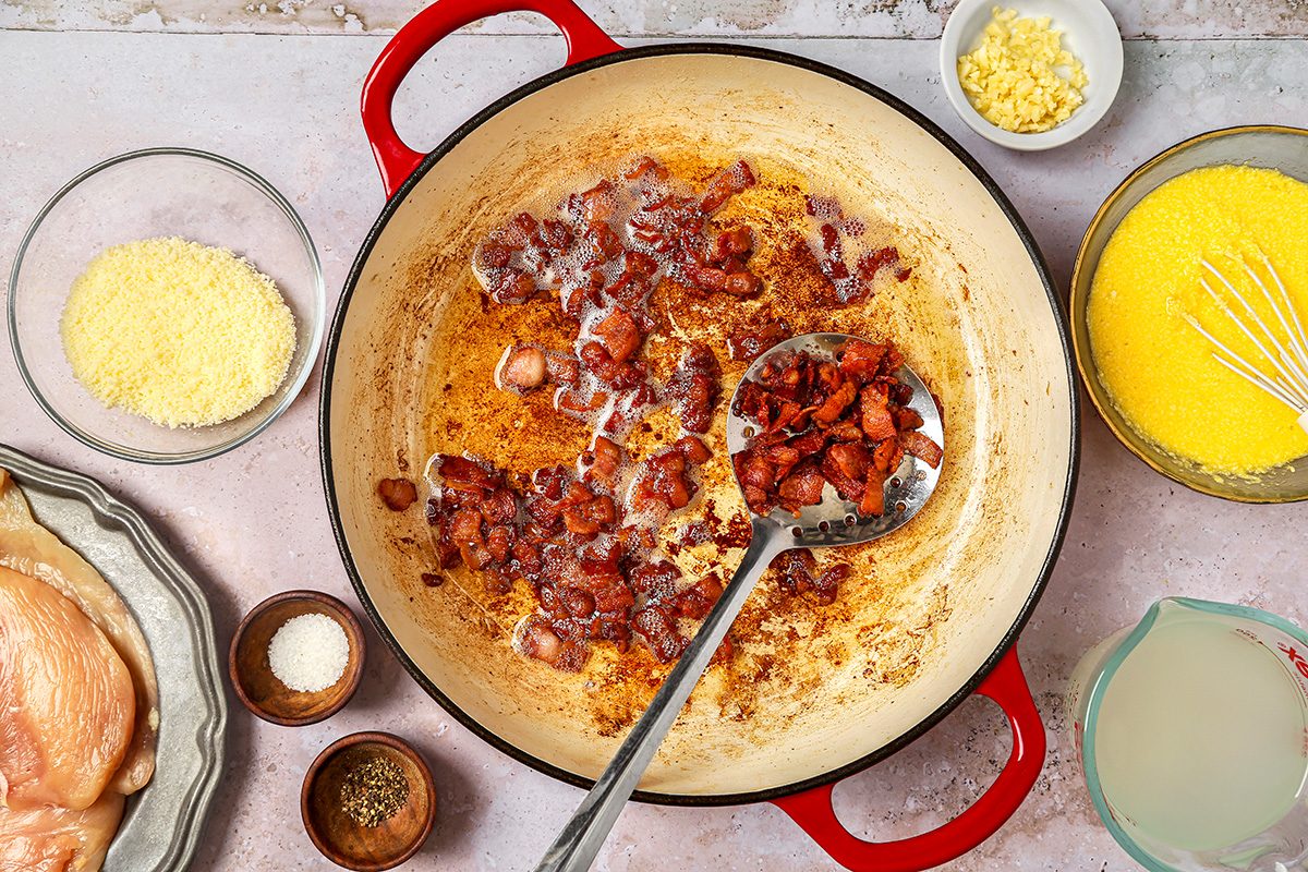overhead shot of round pot with a red handle, which contains sizzling, browned pieces of bacon, frying in some oil