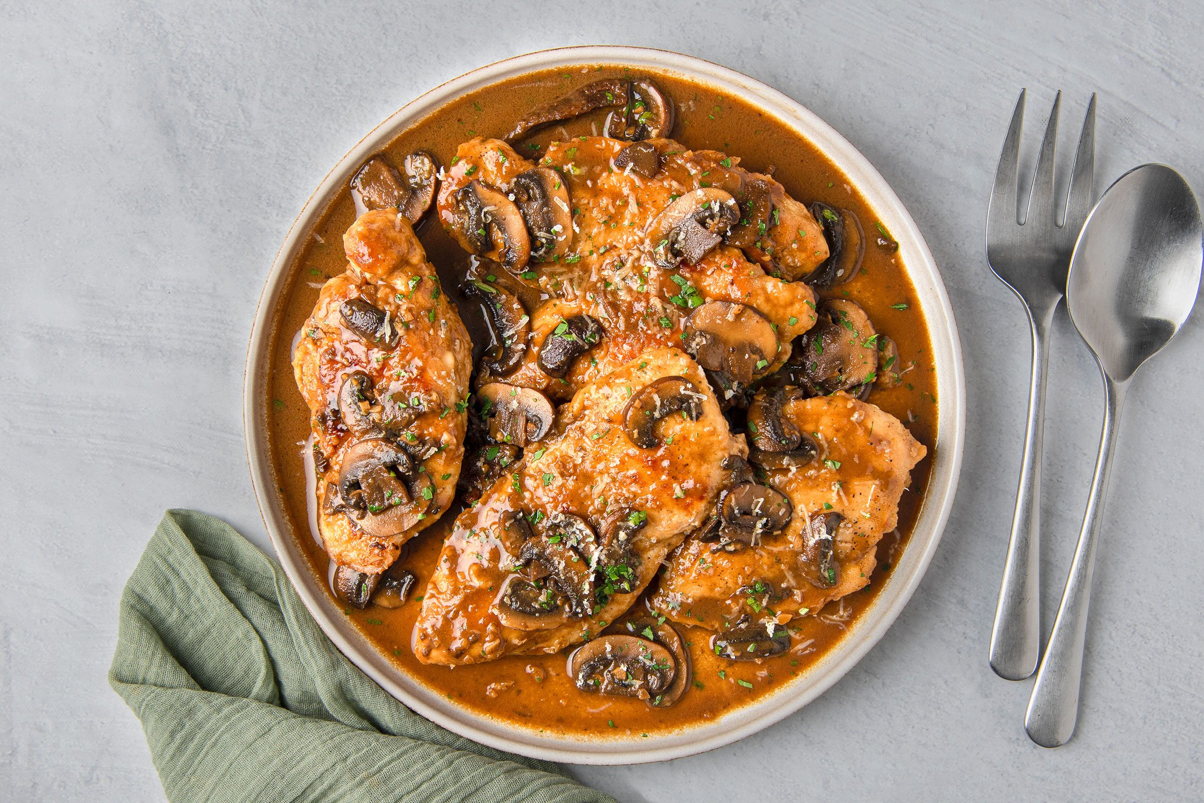 Copycat Olive Garden Chicken Marsala in a white bowl with cutlery placed on side