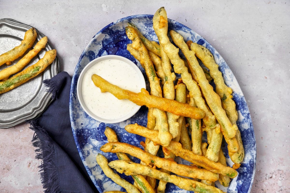 Cover push pull image of Taste of Home's Fried Asparagus recipe shot on a grey concrete surface; Battered and fried asparagus served on a platter with ranch dressing
