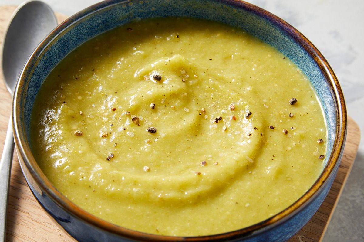 Close-ip shot of Green Enchilada Sauce; served in a bowl; placed over wooden tray with a spoon; all set on a marbel surface