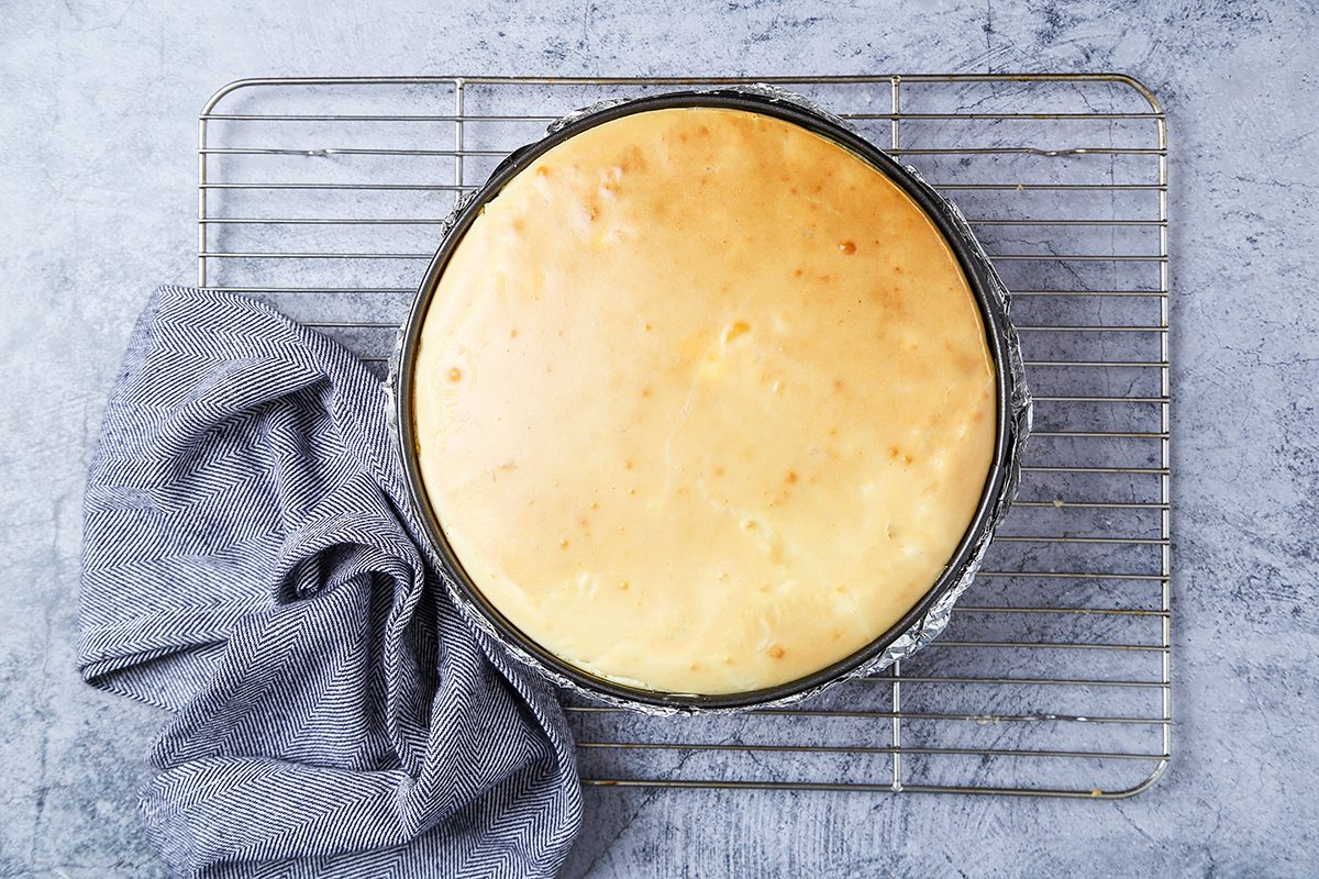Overhead view of a round cheesecake with a golden top, set on a cooling rack. 
