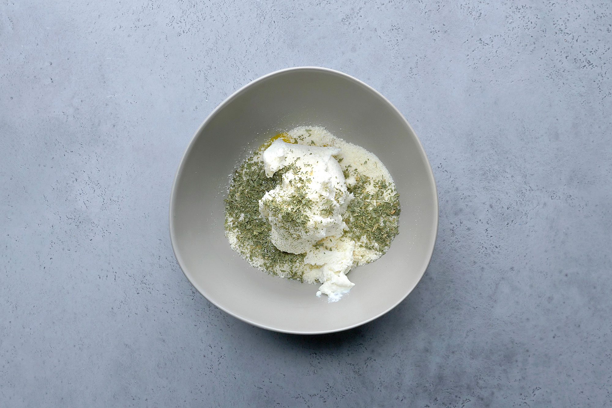 Overhead shot a bowl; mix eggs; ricotta cheese; Parmesan cheese; parsley and pepper; grey surface;