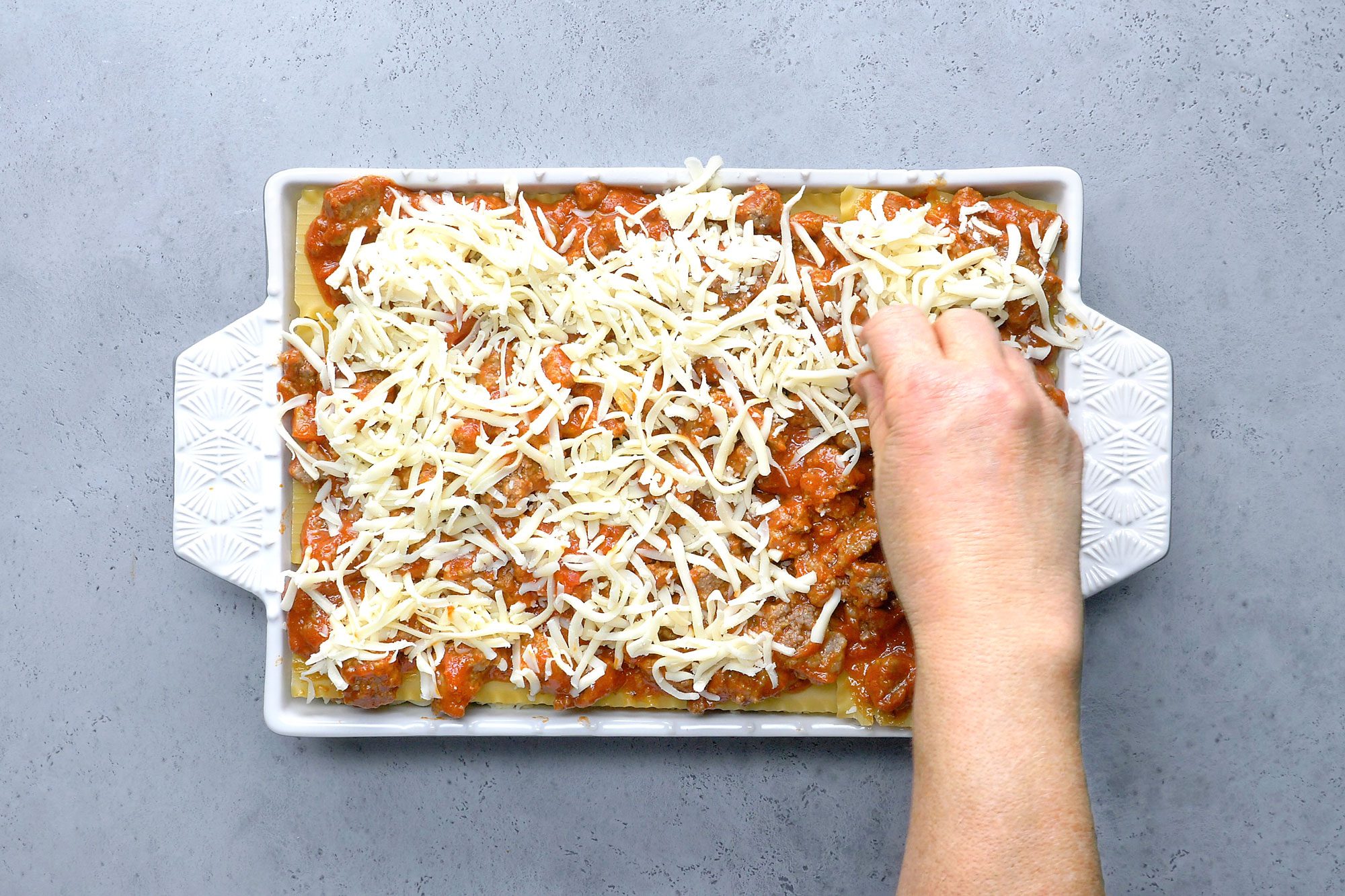 Overhead shot of top with remaining noodles; meat sauce and mozzarella cheese; refrigerate; covered 8 hours or overnight; Preheat oven to 375 degree; remove lasagna from refrigerator while oven heats; bake covered 45 minutes; bake uncovered until cheese is melted 10-15 minutes; Let stand 10 minutes before cutting; grey surface;