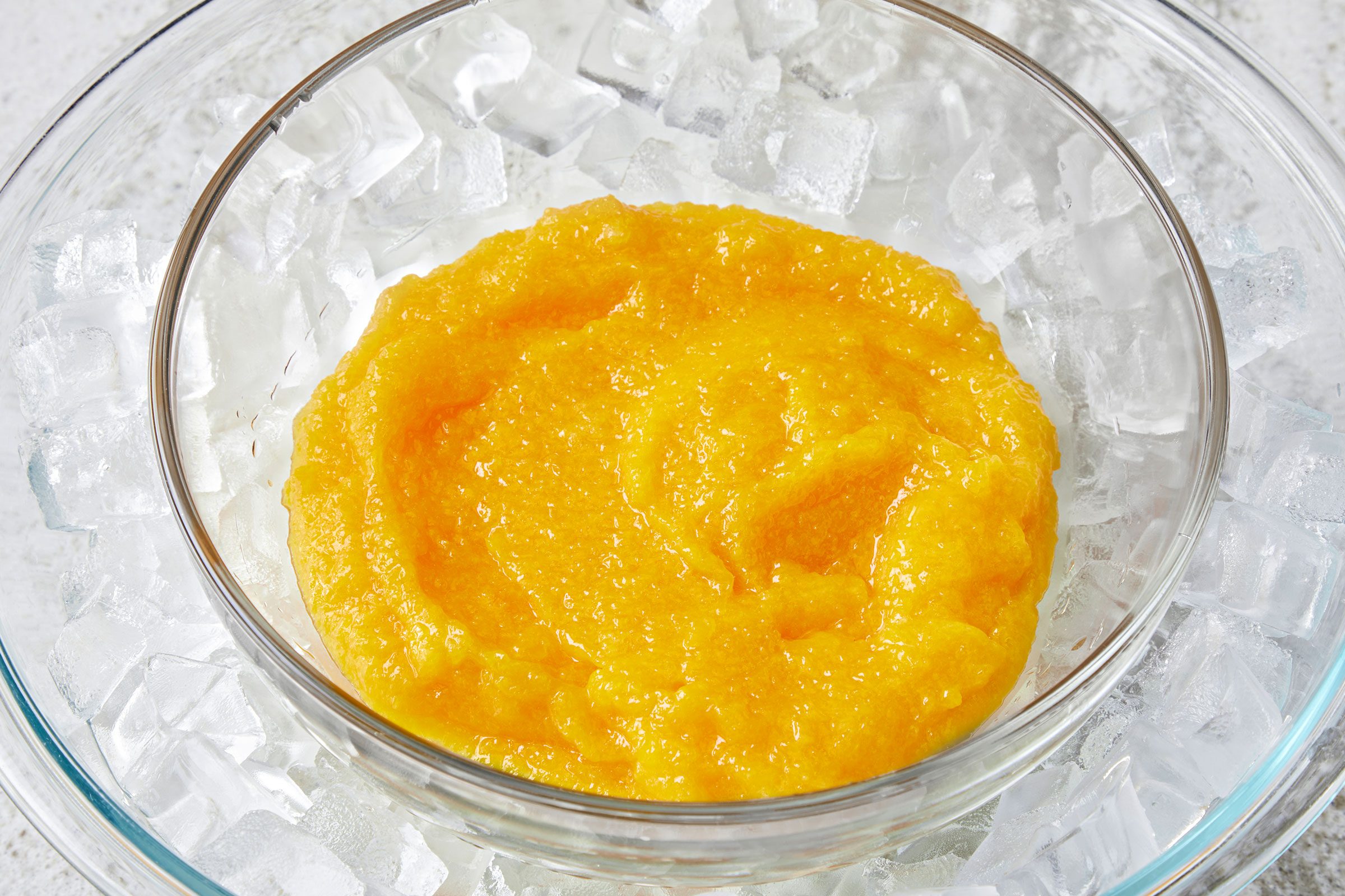 Mango puree into a glass bowl on top of an ice bath in a larger bowl