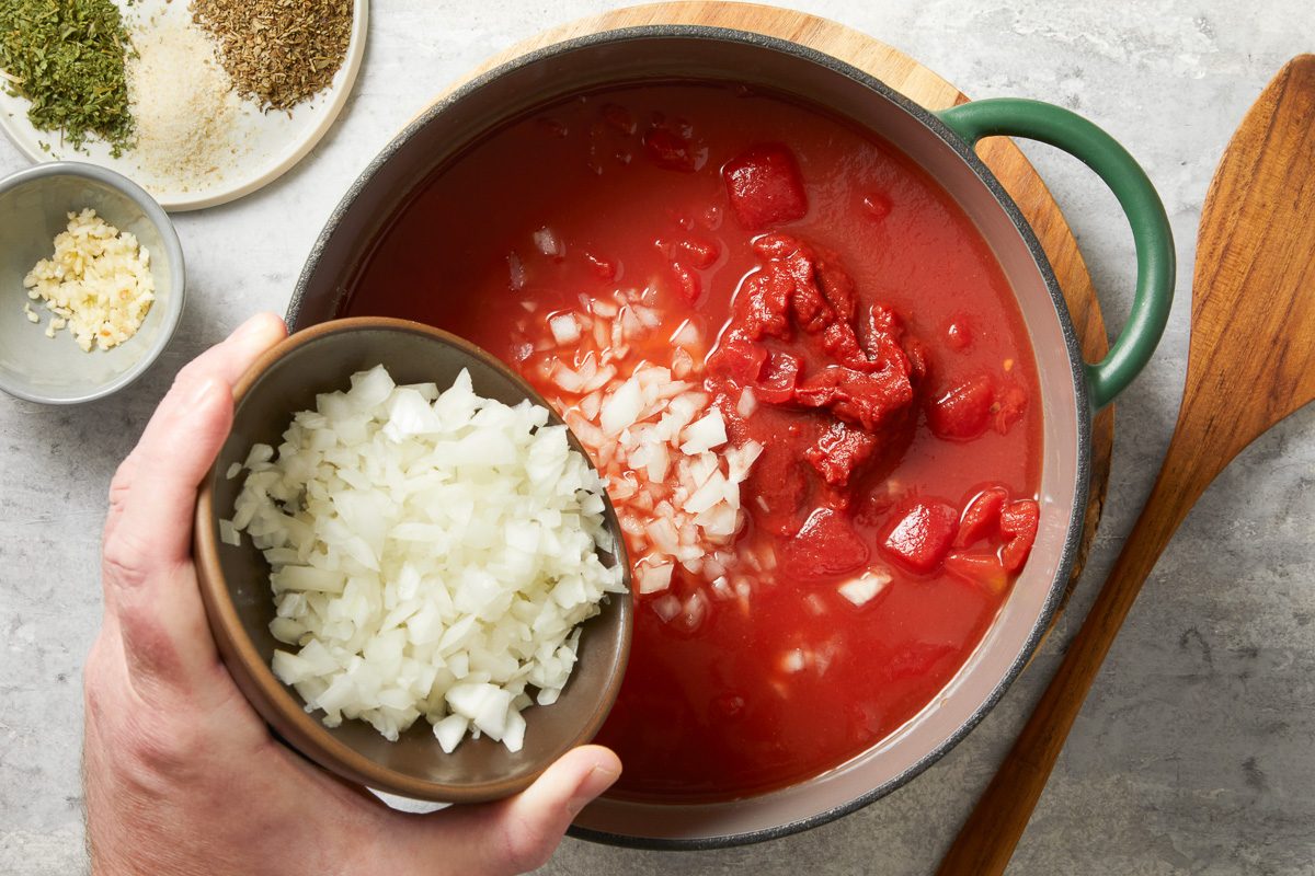onions being added to sauce mixture in saucepan