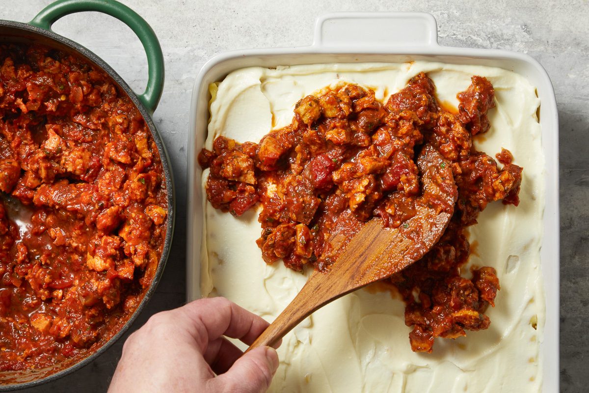 meat sauce being added on top of riccota mix spread