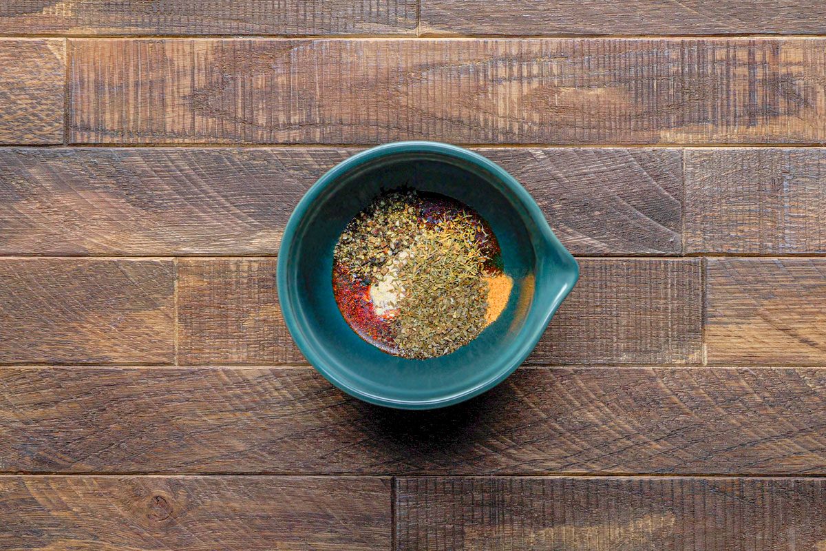 overhead shot of a teal colored bowl filled with various spices on a wooden surface;