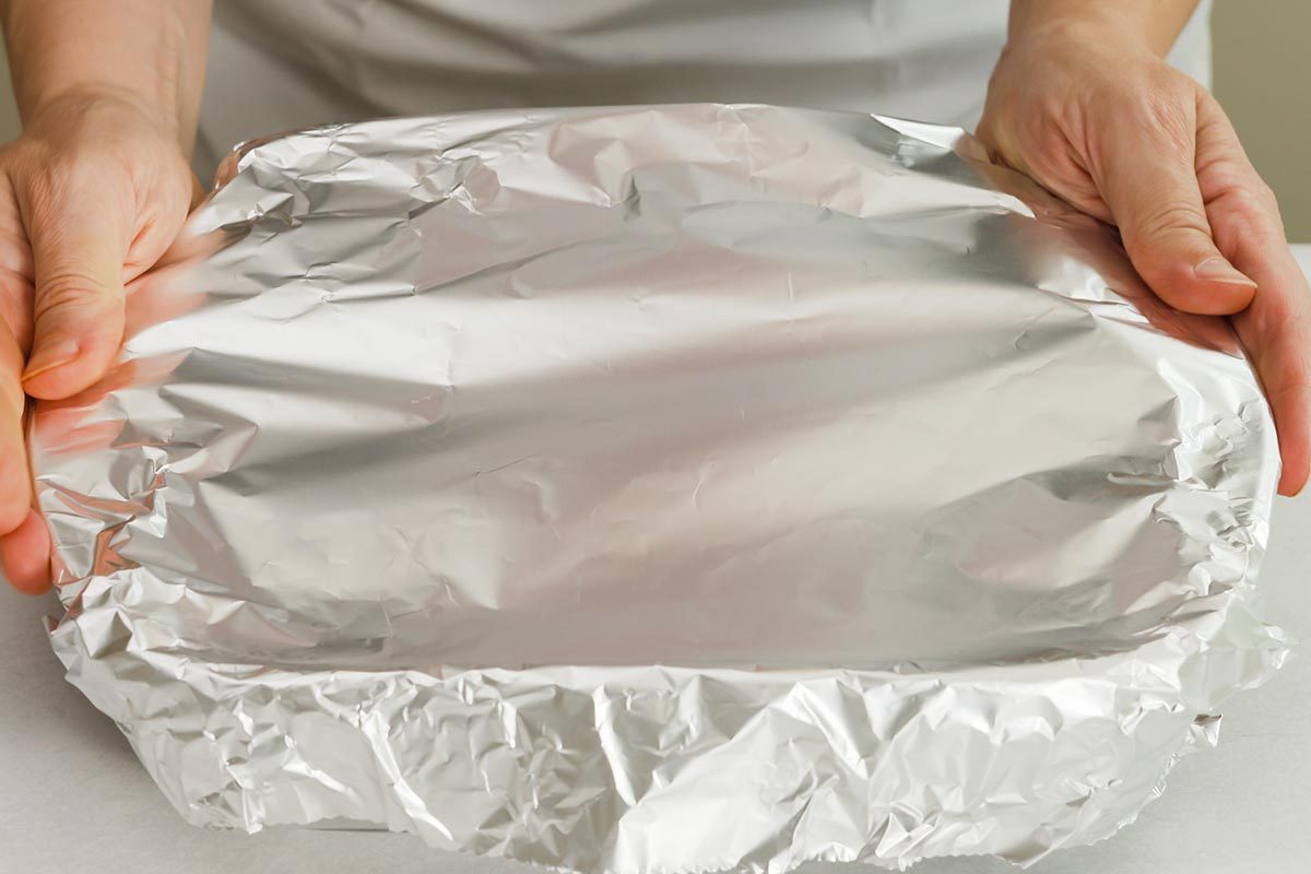 Chef wraps baking pan with aluminum foil.