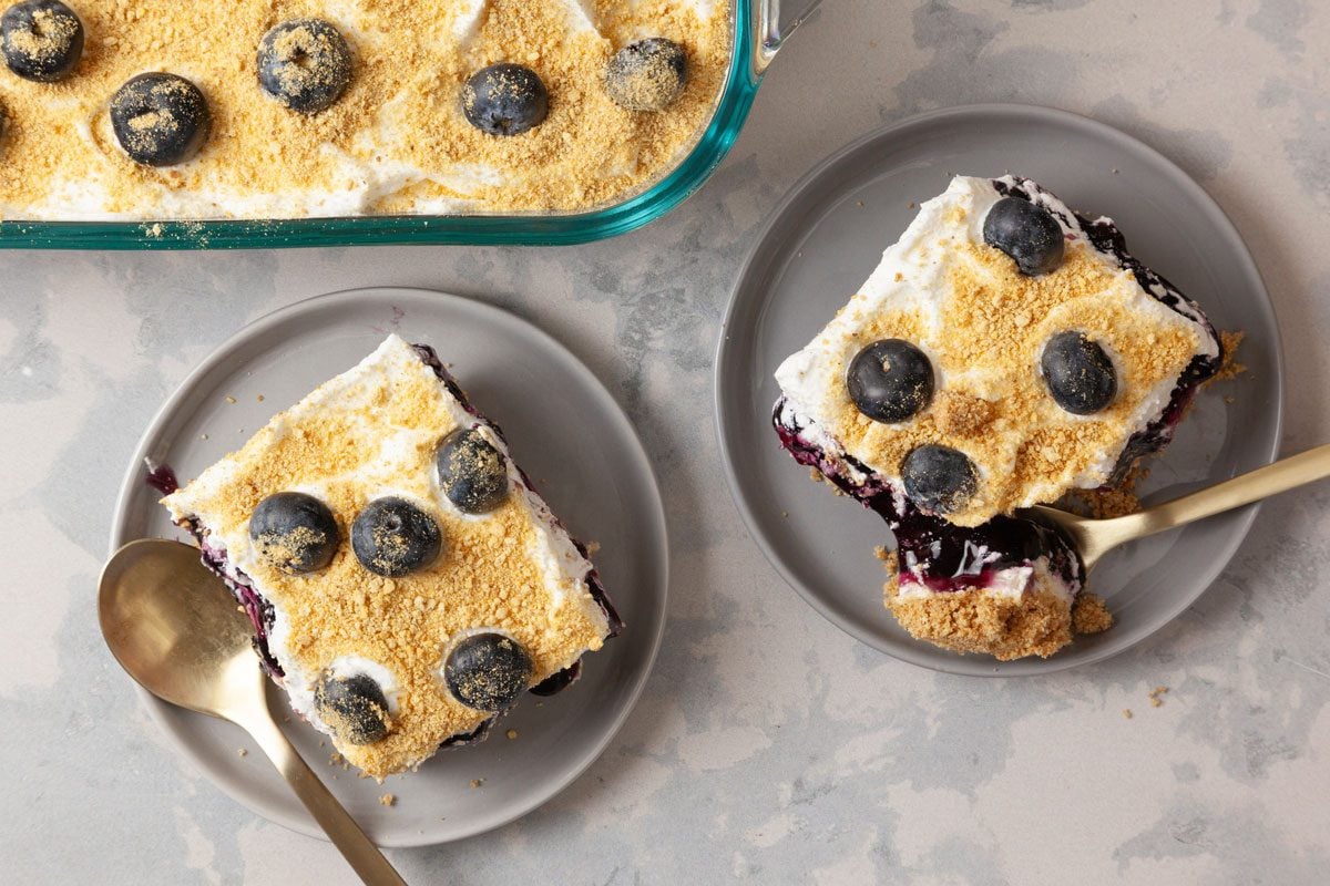overhead shot of Blueberry Delight; beside the main dish, two portions have been served on gray plates, a golden spoon rests next to one of the servings