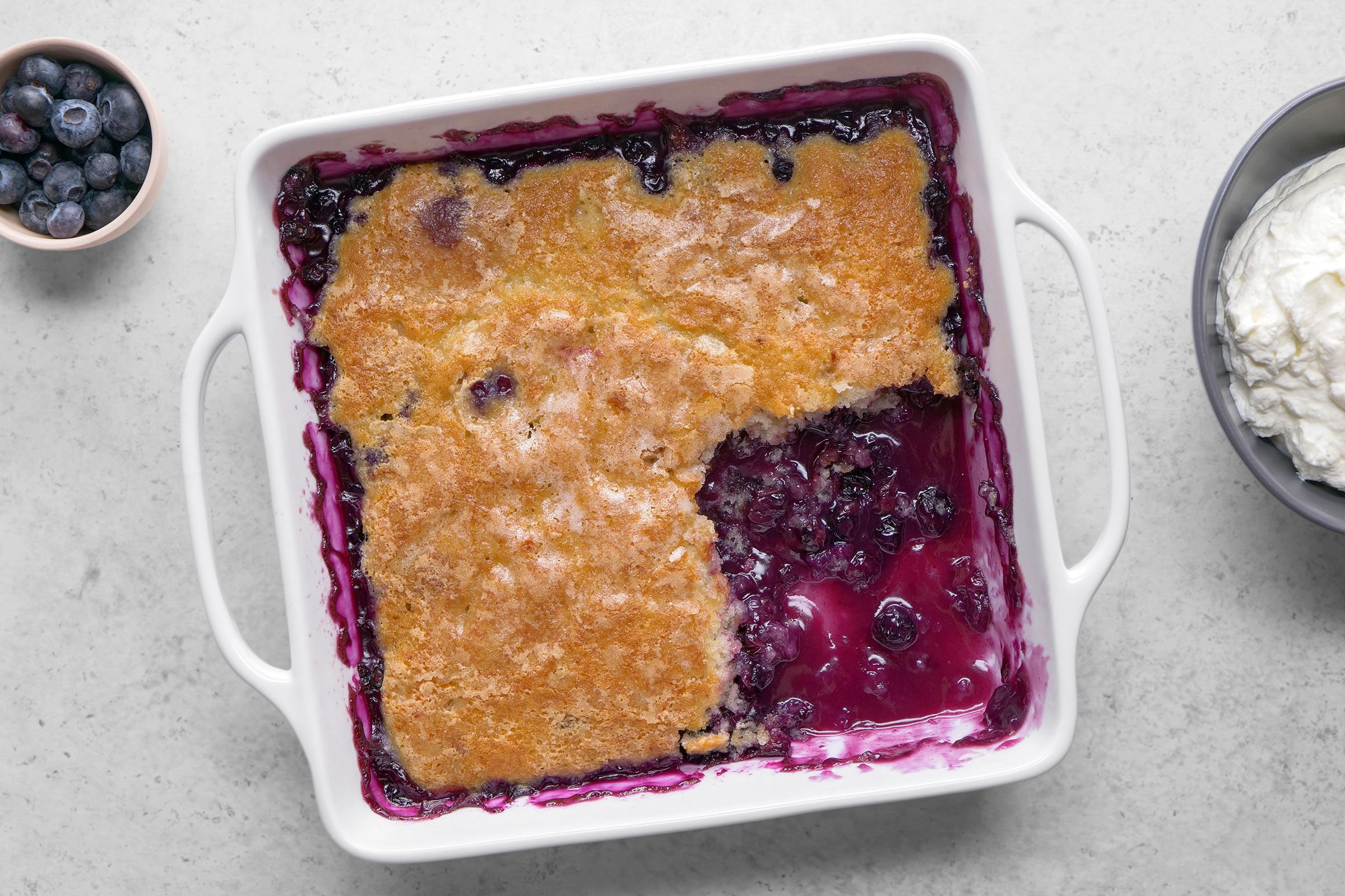 Blueberry Pudding Cake in a baking dish with blueberries on the side
