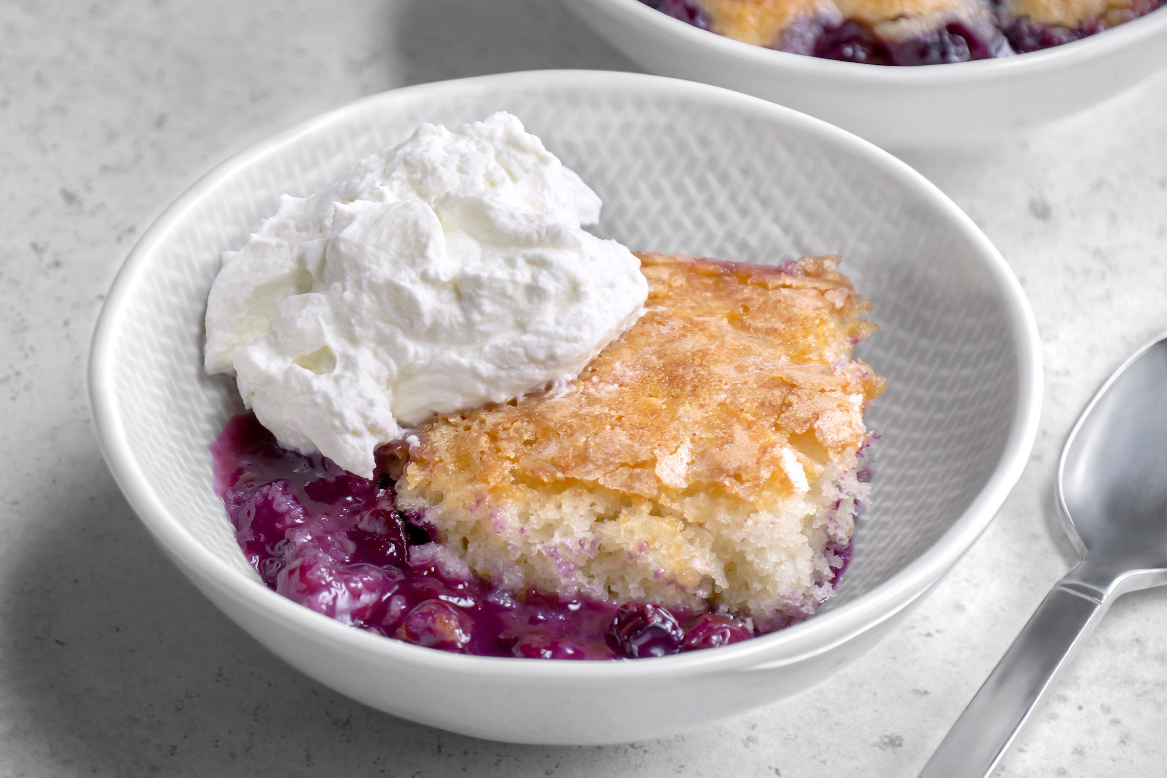 Blueberry Pudding Cake piece in a white bowl with a spoon