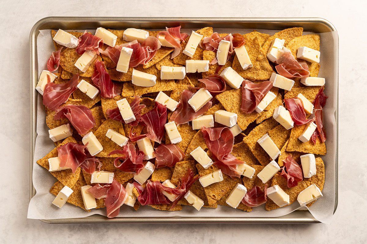 Chips with cubes of brie cheese and slices of cured meat scattered on top
