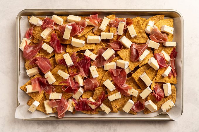 Chips with cubes of brie cheese and slices of cured meat scattered on top