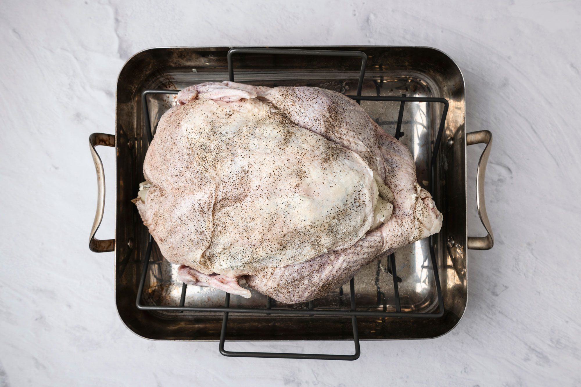 Overhead shot; Preheat oven to 325 degree; Remove giblets from turkey; cover and refrigerate for gravy; Pat turkey dry; place breast side up on a rack in a roasting pan; In a small bowl combine softened butter; thyme and sage; With fingers carefully loosen skin from turkey breast; rub butter mixture under skin; Sprinkle salt and pepper over turkey and inside cavity; fill cavity with celery; onion and carrot; marble surface;