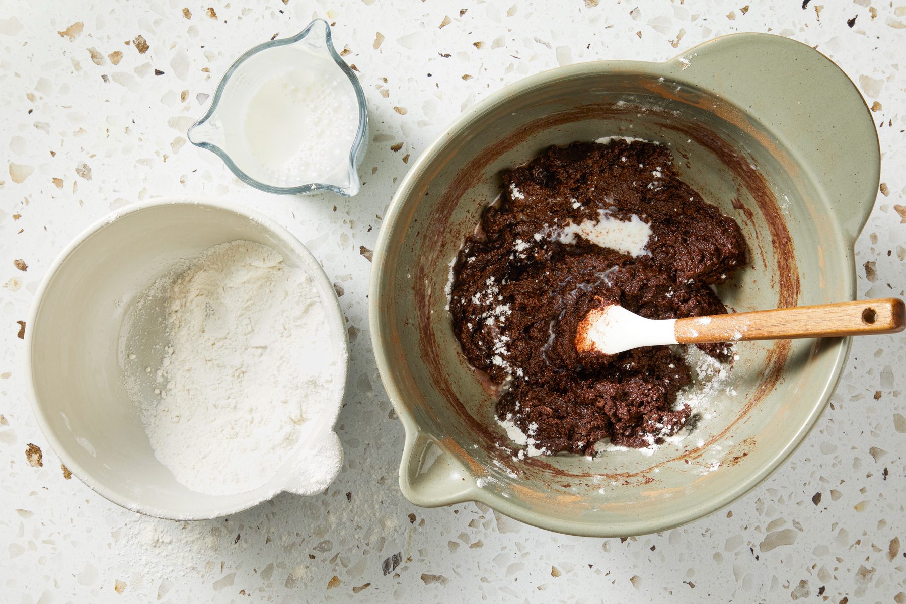 Overhead shot of a small bowl combine flour; baking powder and salt; Alternate adding the dry mixture and milk into the sugar mixture; stir until batter is smoot; spatula; marble surface;