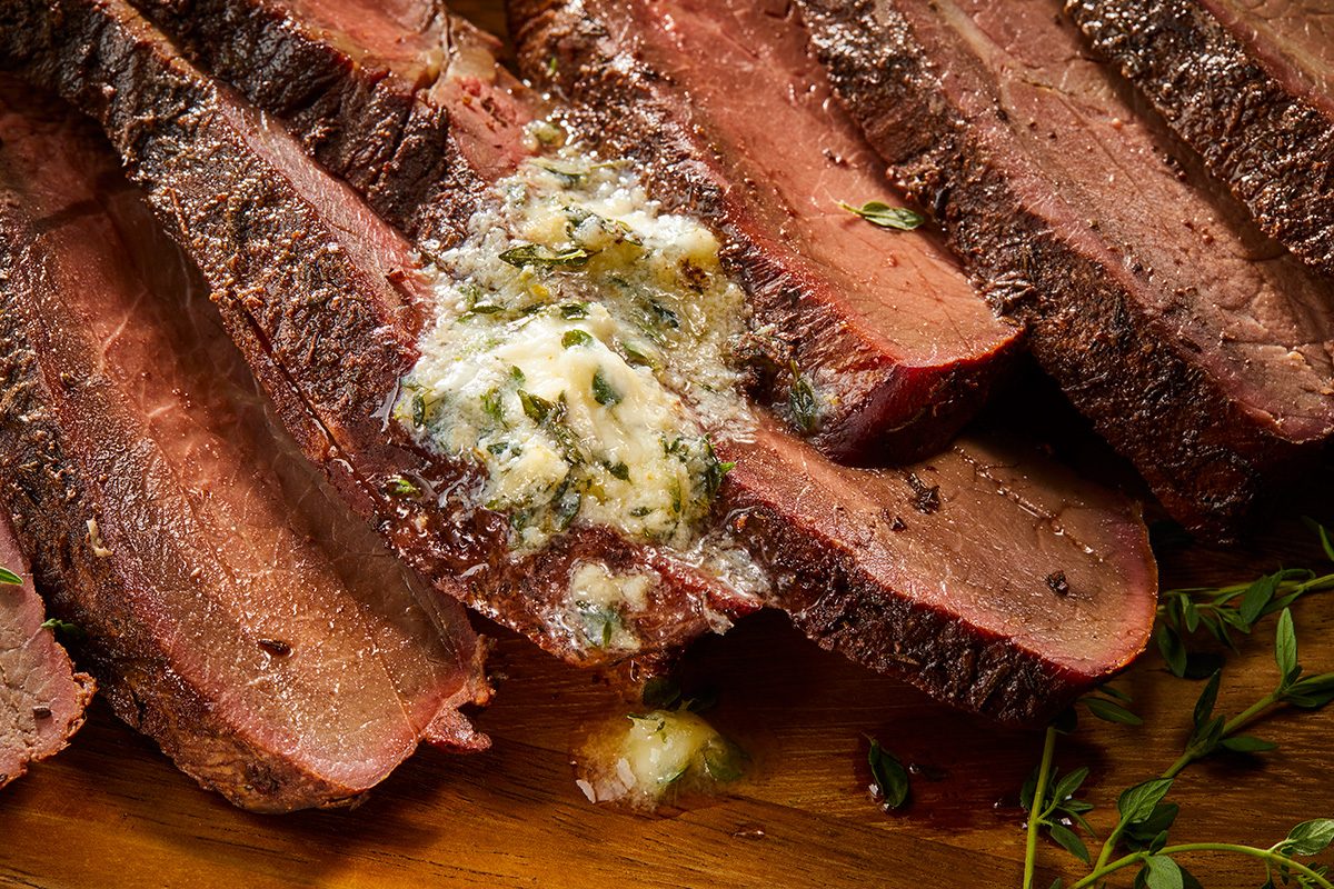 closeup shot of Grilled Sirloin Tip Roast, sliced into thin, even portions, the sliced roast is arranged on a wooden cutting board, garnished with fresh herbs